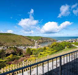 A view from a balcony overlooking a hillside with shrubs and houses by a bay and the ocean at Harbour Lights Port Isaac