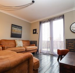 A living room with brown leather sofas a wall clock and a sign near glass doors at Hillcroft in St Austell