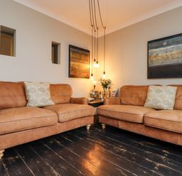 A living room with two brown leather sofas a side table with flowers and hanging lights at Hillcroft in St Austell