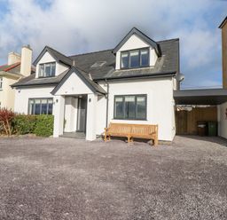 A white two-story house with a porch and bench in front at Tarth Y Mor in Criccieth