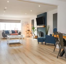 A living room with a gray sofa a white coffee table a blue armchair a fireplace and a dining table with metal chairs at Tarth Y Mor in Criccieth