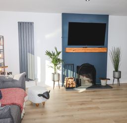 A living room with a gray sofa, a sheep-shaped footstool, plants on stands, a fireplace with firewood, and a mounted television at Tarth Y Mor in Criccieth