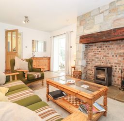 A living room with an armchair and sofa facing a stone fireplace with a wood stove at Canny Cottage Low Hauxley Nr Amble