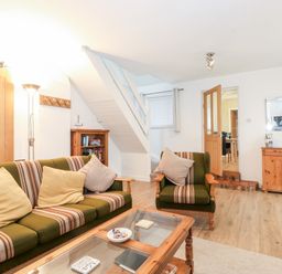 A sitting room with a striped green sofa and armchair a wooden coffee table a wooden sideboard and a bookshelf at Canny Cottage Low Hauxley Nr Amble