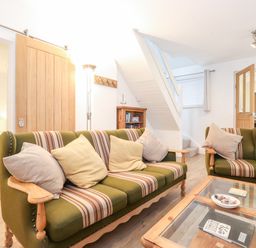 A living room with green striped sofas, a glass coffee table, wooden doors, a staircase, and a bookshelf at Canny Cottage Low Hauxley Nr Amble
