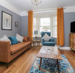 A living room with a brown sofa blue armchair wooden coffee table patterned rug and wooden chest of drawers at Cornerside in Sidmouth
