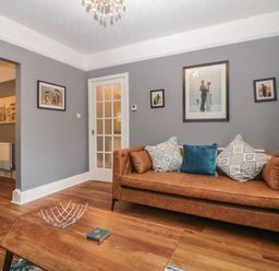 A living room with a brown sofa and cushions a wooden coffee table with a metal centerpiece and wall art at Cornerside in Sidmouth
