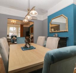 A dining room with a wooden table and upholstered chairs with a large mirror on a blue accent wall at Cornerside in Sidmouth