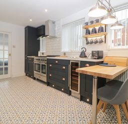A kitchen with black cabinets a stainless steel oven wooden countertop and patterned floor tiles at Cornerside in Sidmouth