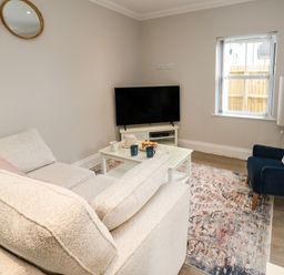 A living room with a beige sofa a blue armchair a white coffee table with cups and plate a television on a white stand two round mirrors on the wall and a window at 3 Compass Point Weymouth