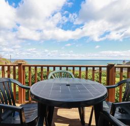 An outdoor wooden deck with a round plastic table and four chairs overlooking the sea at Beachcliff in Gorran Haven