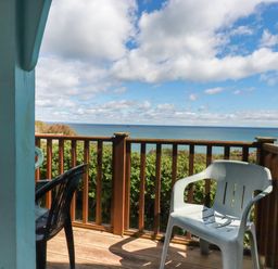 A balcony with plastic chairs and wooden railing overlooking the ocean at Beachcliff in Gorran Haven