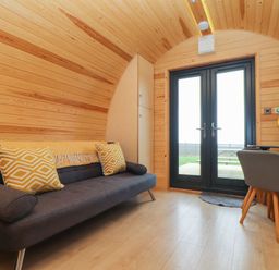 A wooden room with a sofa, pillows, a small table with chairs, and double glass doors at Sun Rise in St Buryan