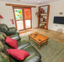 A living room with green leather sofas red cushions a wooden coffee table a floor lamp a wooden shelving unit and a wall-mounted TV at Nook Bethesda near Narberth