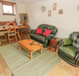 A living room with green leather sofa and armchair wooden coffee table and dining table with chairs at Nook Bethesda near Narberth