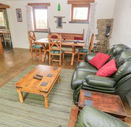 A living area with a green leather sofa red cushions a wooden coffee table with remotes and a dining table with wooden chairs at Nook Bethesda near Narberth