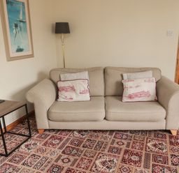 A beige sofa with patterned cushions next to a small side table and standing lamp in a room at Causeway Cottage in Holy Island