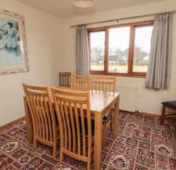 A dining room with a wooden table and six chairs next to a window with grey curtains at Causeway Cottage in Holy Island