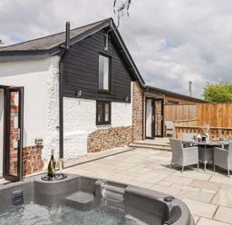 An outdoor patio with a hot tub a table with chairs and a house with open doors at Strawberry Bank - Kingfisher in Pyworthy near Bridgerule
