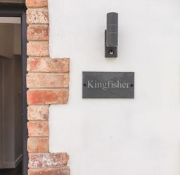 A wall with a black outdoor light fixture and a sign that reads Kingfisher next to a partially open door