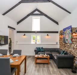 A living room with a dining table set for four and a black sectional sofa against a stone wall at Strawberry Bank - Kingfisher in Pyworthy near Bridgerule