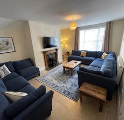 A living room with two blue sofas a wooden coffee table a fireplace with a TV above and a patterned rug at The Hame in Monmouth