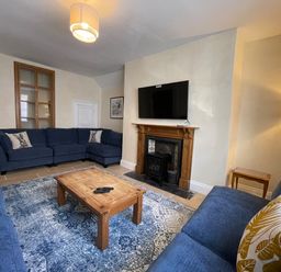 A living room with blue sofas a wooden coffee table a fireplace with a mounted television and a standing lamp at The Hame in Monmouth