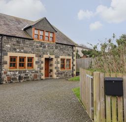 A stone house with wooden framed windows a gravel driveway and a wooden gate at Whin Hill Cottage in Craster