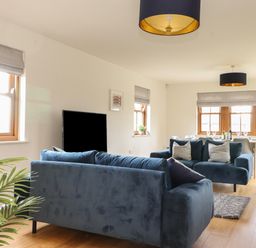 A living room with two blue sofas a television and a dining table with chairs at Whin Hill Cottage in Craster
