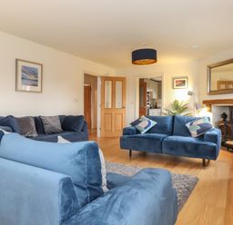 A living room with blue sofas a wood stove a TV and wooden flooring at Whin Hill Cottage in Craster