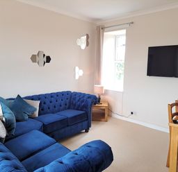 A living room with blue sectional sofa cushions TV on wall and a wooden dining table with chairs at Bogrie Cottage Canonbie near Gretna Green