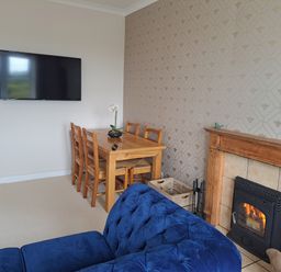 A dining table with chairs next to a wall mounted TV and a fireplace with a blue sofa in the foreground at Bogrie Cottage Canonbie near Gretna Green