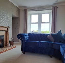 A living room with a blue sectional sofa and a fireplace near a window at Bogrie Cottage in Canonbie near Gretna Green