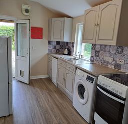 A kitchen with white cabinets appliances and patterned tile backsplash at Bogrie Cottage in Canonbie near Gretna Green