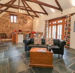 A living area with a black sofa and wooden coffee table near a kitchen and stone wall at The Threshing Barn in Highampton