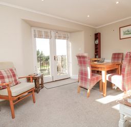 A dining area with a wooden table and four red plaid chairs next to double doors and an armchair with a red plaid cushion at Magnolia House in Dittisham