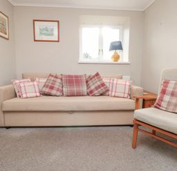 A living room with a beige sofa and checkered cushions next to an armchair with a cushion and a window with a lamp on the sill at Magnolia House in Dittisham