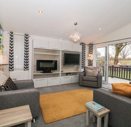 A living room with gray sofas an orange rug a wall-mounted TV and large windows opening to a garden at Owls Nest in Furzehill