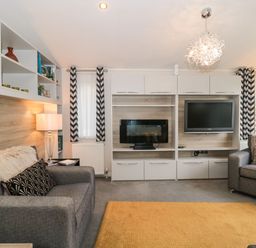 A living room with two gray sofas a wall unit with a television and electric fireplace and patterned curtains at Owls Nest in Furzehill