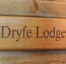 A wooden sign with the text Dryfe Lodge mounted on a wooden surface at Dryfe Lodge in Lockerbie
