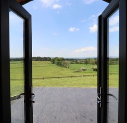 A view of green fields and trees through open glass doors at Dryfe Lodge in Lockerbie