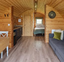 An interior view of a wooden cabin with a kitchen area dining table sofa and a bedroom visible at Dryfe Lodge in Lockerbie
