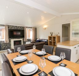 A dining area with a wooden table set for six people and a living room with a sofa and wall-mounted TV at Lake View Lodge in Lakeside 3 White Cross Bay Windermere
