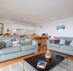 A living room with two sofas a black coffee table and a kitchen area with bar stools at Fistral Pearl in Newquay