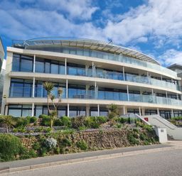 A modern apartment building with glass balconies and landscaped gardens in front at Fistral Pearl in Newquay