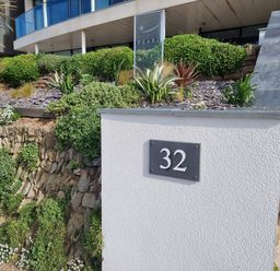 An outdoor area with a white wall displaying the number 32 stone steps and green plants at Fistral Pearl in Newquay