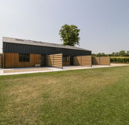 A modern barn style building with wooden and metal siding next to a grassy lawn at Basswood Barn in Lime Tree Barn