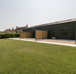 A modern black building with three paved outdoor spaces and a lawn at Basswood Barn in Lime Tree Barn