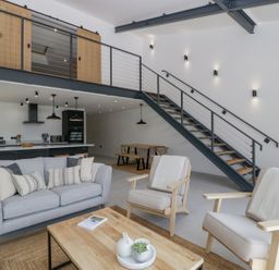 A living room with sofa and armchairs next to a wooden coffee table and a dining area under a staircase at Basswood Barn in Lime Tree Barn
