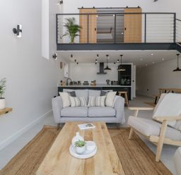 A living room with a gray sofa two armchairs and a wooden coffee table with plants and a book at Basswood Barn in Lime Tree Barn